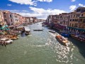 Kto z nas choć raz nie marzył o wycieczce do miasta gondoli, mostów, kolorowych masek i karnawału? Wenecja (wł. Venezia) od lat stanowi „obiekt” pożądania wielu turystów, którzy zauroczeni zdjęciami miasta obiecują sobie przybycie tutaj choćby na jeden dzień.

O lokalizacji Wenecji można powiedzieć, że jest niezwykła - miasto położone jest na wodzie, tworzone przez zespół wąskich uliczek i wszechobecnych kanałów, które decydują o tutejszym transporcie. Wenecja to nie tylko miasto, ale również gmina w północnych Włoszech, nad Morzem Adriatyckim. 


Historia


Historia miasta rozpoczyna się w 452 r. kiedy to grupa uciekinierów osiedliła się w pobliżu dzisiejszej Wenecji. Władzę w rozwijającym się mieście-państwie sprawował wówczas doża (dziś możemy podziwiać m.in. Pałac Dożów), wybierany do pełnienia swojego urzędu dożywotnio. Wenecjaniemal od początku swego istnienia była obszarem wielonarodowościowym oraz stanowiła centrum, które posiadało wpływy w wielu miejscach na obszarze Morza Śródziemnego (Wyspy Egejskie, Cypr, Kreta oraz wiele innych). Wiążąca się z różnorodną kulturą wieloreligijność, stała się punktem zapalnym w sporze z Rzymem, który przerodził się w oficjalny konflikt. Po trwających kilka wieków problemach natury handlowej, Wenecja utraciła swoją dotychczasową mocną pozycję na arenie międzynarodowej. W 1797 r. została zdobyta przez Napoleona i tym samym włączona do państwa austriackiego (na mocy pokoju w Campo Formio w tym samym roku). Dopiero od XIX stanowi część Włoch.


Atrakcje turystyczne


Ciężko wymienić wszystkie atrakcje i zabytki, jakie czekają na turystów po przybyciu do Wenecji. Zasadniczo najwięcej z nich pochodzi z okresu między XIII a XVI w., kiedy miasto rozwijało się najprężniej. Ślady św. Marka, patrona Wenecji, widoczne są niemal na każdym kroku (np. bazylika św. Marka). Miasto zostało wpisane na Listę Światowego Dziedzictwa UNESCO, warto zobaczyć choć część jego zabytków i niespodzianek.

Spotkajmy się na Placu św. Marka - można najczęściej usłyszeć w Wenecji. To centralne miejsce stanowi punkt orientacyjny, zdawałoby się, że wszystkie ulice prędzej czy później doprowadzą nas właśnie tutaj. Plac św. Marka (Piazza San Marco) związany jest z budową bazyliki św. Marka w IX w., początkowo znacznie mniejszy i podzielony przez jeden z kanałów, kształt obecny uzyskał dopiero w XII w. Wokół placu znajduje się szereg kawiarni, restauracji oraz drobnych sklepików z pamiątkami, obok których wznoszą się największe atrakcje miasta - m.in. bazylika św. Marka z dzwonnicą, wieża zegarowa (Torre dell'Orologio), Pałac Dożów, dwa budynki Prokuracji (Stara i Nowa Prokuracja) oraz łączące je klasycystyczne skrzydło Ala Napoleonica. Skrzydło, stanowiące nie tylko łącznik pomiędzy Prokuracjami, jest przede wszystkim siedzibą kilku ważnych muzeów: Museo Correr (zbiory dotyczące historii miasta), Quadreria (malarstwo weneckie), Museo Archeologoco (Muzeum Archeologiczne), Museo del Risorgimento (eksponaty dotyczą powstania z 848 r.). Bazylika św. Marka znajdująca się niemalże na wszystkich pocztówkach z Wenecji, została wybudowana dla pochowania relikwii ewangelisty - patrona miasta. Świątynia powstała w latach 828-832, w 976 r. spłonęła podczas pożaru. Obecny kształt jest wynikiem odbudowy zakończonej w 1094 r. Wnętrze bazyliki zdobią liczne, cenne mozaiki, rzeźby (z najsłynniejszą - kwadrygą koni z brązu, wykonaną prawdopodobnie w II w. p.n.e.), obrazy, marmurowe kolumny.

Wizytówką miasta jest również Pałac Dożów - równie rozpoznawalny jak Plac św. Marka. Powstała w gotyku budowla służyła przed wiekami za siedzibę władców weneckich, spełniała również funkcje obronne. W pałacu uwagę przyciągają m.in. Schody Gigantów, piękne arkadowe loggie, rzeźby, figury, obrazy, posągi antycznych bogów, freski Veronesego oraz dziedziniec łączący się z bazyliką św. Marka. Na najwyższym piętrze pałacu mieściło się więzienie Piombi, którego „gośćmi” byli m.in. Giacomo Casanova oraz Giordano Bruno.

Charakterystyczna wieża zegarowa przy Placu św. Marka została zaprojektowana przez uzdolnionego Maura Codussiego i powstała na przełomie XV i XVI w. Poza klasycznym odmierzaniem czasu (na szczycie wieży dwóch Maurów (posągi) uderza w potężny dzwon co godzinę) atrakcją jest także zegar astronomiczny, pokazujący pory roku i fazy księżyca.

Pięknie zdobiony jest również trójnawowy kościół San Giorgio Magiorre na wyspie San Giorgio wzniesiony w między 1597 a 1610 r. W jego wnętrzu podziwiać można grobowce dożów oraz drogocenne malowidła, z których najcenniejsza jest Ostatnia wieczerza Tintorettego. Turyści chętnie odwiedzają również niewielką bazylikę Santa Maria Della Salute, wzniesioną po epidemii dżumy, która zdziesiątkowała populację Wenecji. Świątynia projektu Longhena znajduje się przy kanale Grande, w jej wnętrzu można podziwiać m.in. obrazy Tycjana oraz Tintorettego.

Wenecja kojarzy się wszystkim z mostami. Najbardziej znany z nich - Most Westchnień - zbudowany został w 1614 r. To właśnie tędy więźniowie byli prowadzeni do cel. Według legendy (którą w dużej mierze upowszechnili lokalni poeci) skazańcy przechodząc przez most wzdychali za utraconą wolnością oraz ukochanymi kobietami - tak miała powstać nazwa mostu. Drugim, najbardziej rozpoznawalnym po Moście Westchnień, jest Rialto wznoszący się nad Kanałem Grande. Most ma długość 28 metrów i jest siedzibą licznych straganów z pamiątkami - podczas wizyty w Wenecji nie sposób nie przepłynąć gondolą i nie kupić karnawałowej maski.

To tylko mała część zabytków i atrakcji, jakie czekają nas po przybyciu do „miasta na wodzie”. Zagłębiając się w korytarze wąskich uliczek (czasem można się tutaj zgubić) sami poznamy, co jest warte zobaczenia. Niemal na każdym kroku Wenecja urzeka swoją architekturą i specyficznym klimatem.


Noclegi


Biorąc pod uwagę fakt, że Wenecja leży na 118 niewielkich rozmiarów wyspach, na usta ciśnie mi się stwierdzenie, że tutejsza baza noclegowa znacznie wykracza poza normę. Hoteli i tanich pensjonatów mamy tu na pęczki, do tego dochodzą prywatne kwatery, apartamenty, schroniska, itp. Jest więc w czym przebierać. Do tych z „wyższej półki” zaliczyć można luksusowy, nowocześnie urządzony, 5-gwiazdkowy hotel The Excelsior, Venice Lido Resort, Centurion Palace, Metropole, Hotel Danieli czy Hilton Molino Stucky Venice. Zaledwie o gwiazdkę niżej plasują się San Cassino Ca’Favretto, Una Hotel Venezia, Royal San Marco, Bucintoro, Santa Marina, Al Codega. Zdecydowanie tańszy nocleg znajdziemy bez wątpienia w hotelu Florida, Falier, Rivamare, Tivoli, Leonardo, Adua, Al Piccolo, Montepiana, Alex, Casa Boccassini, Biasin, Doni, Rossi - wymieniać można by bez końca, możliwości noclegowe w Wenecji są naprawdę imponujące.


Pogoda


Klimat i pogoda panująca w Wenecji sprzyja zwiedzaniu miasta. Lato nie należy tutaj do upalnych (około 23°C), zimą średnio 4°. Śnieg nie powinien nas zaskoczyć, pada tutaj wyjątkowo rzadko. Większych opadów deszczu możemy natomiast spodziewać się w okolicach października i listopada. Na przełomie jesieni i zimy następuje znaczny wzrost wody w kanałach, które powodują zalanie Placu św. Marka (ustawiane są specjalne podesty, które umożliwiają turystom i mieszkańcom poruszanie się po placu).